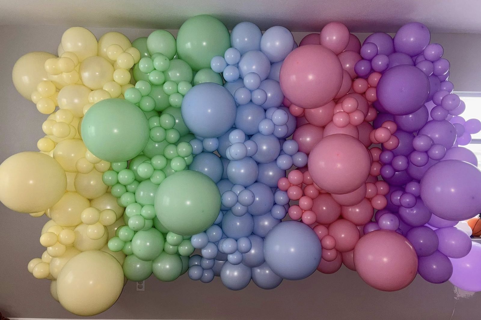 Full pastel rainbow balloon wall in yellow, mint, blue, pink, and purple